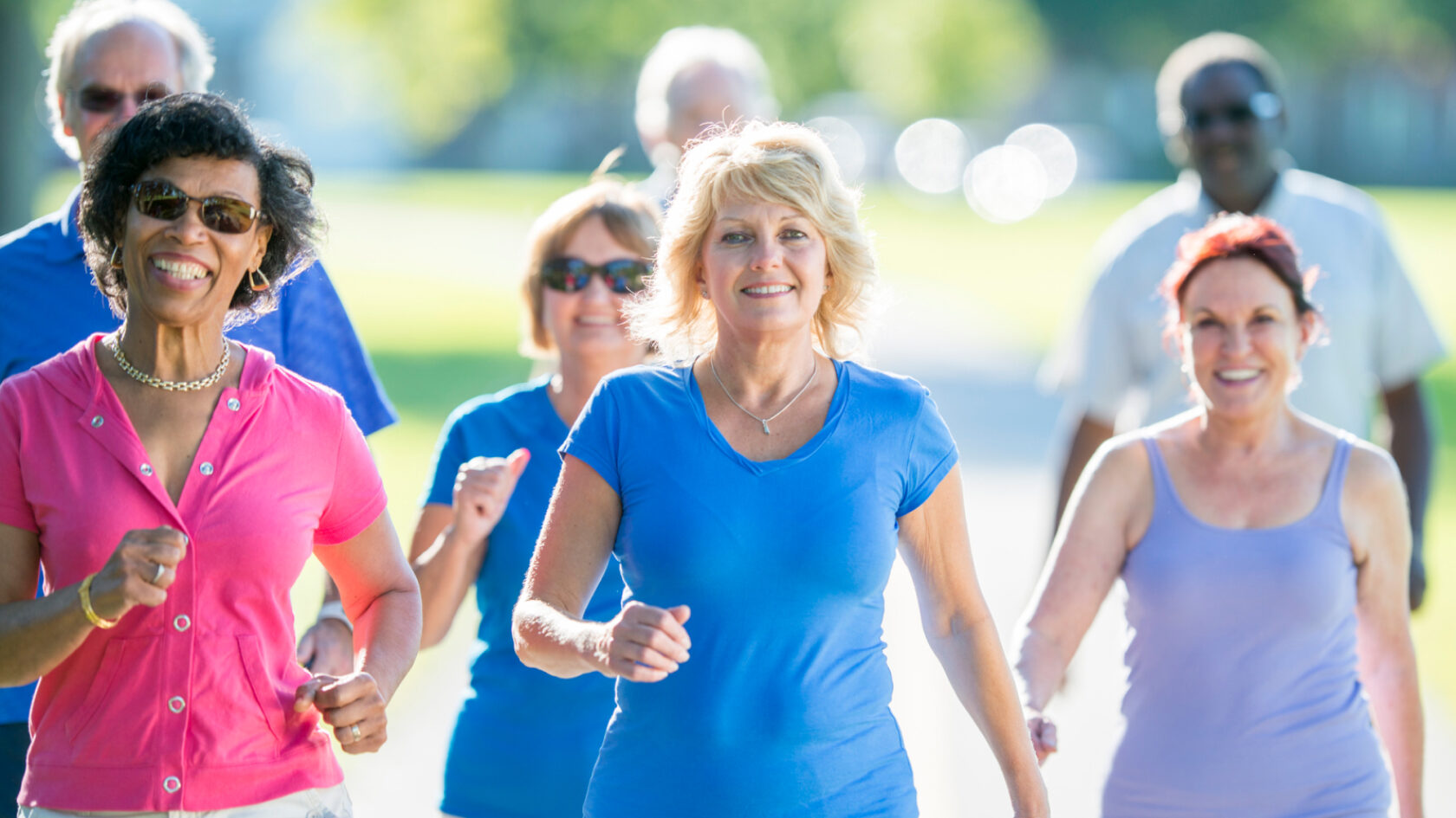 A group of exercisers take a walk outside in the sun.