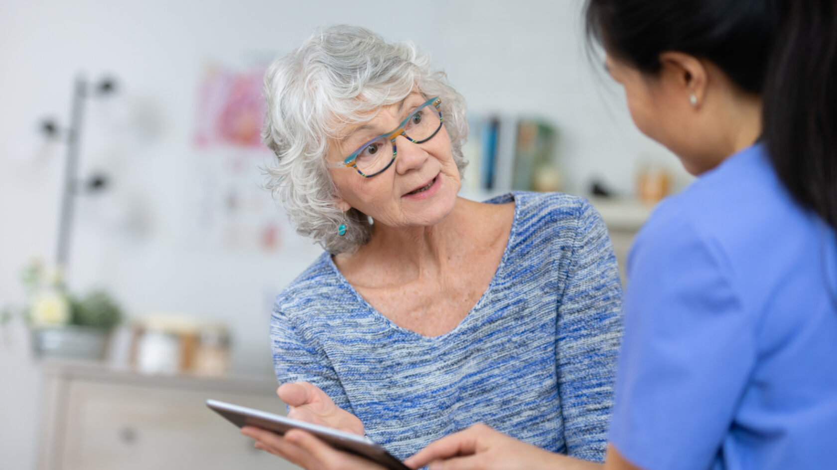 A woman reviews her health information on a tablet with a clinician.