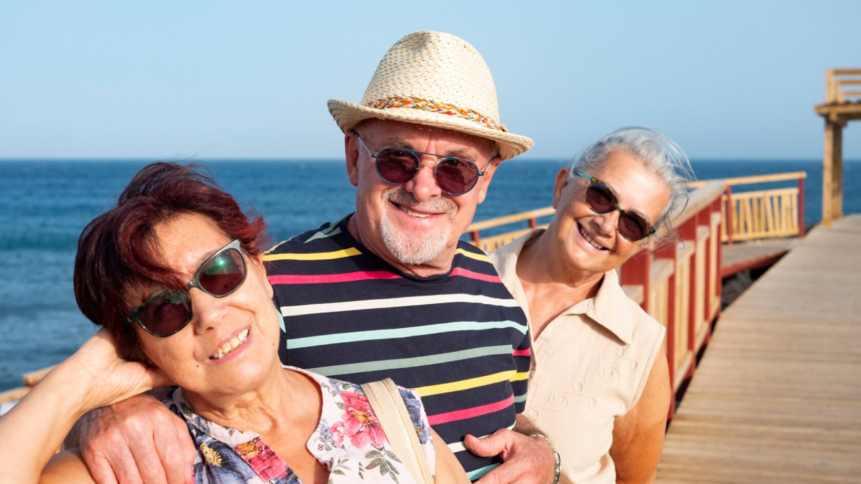 Three friends pose for a picture on a boardwalk.