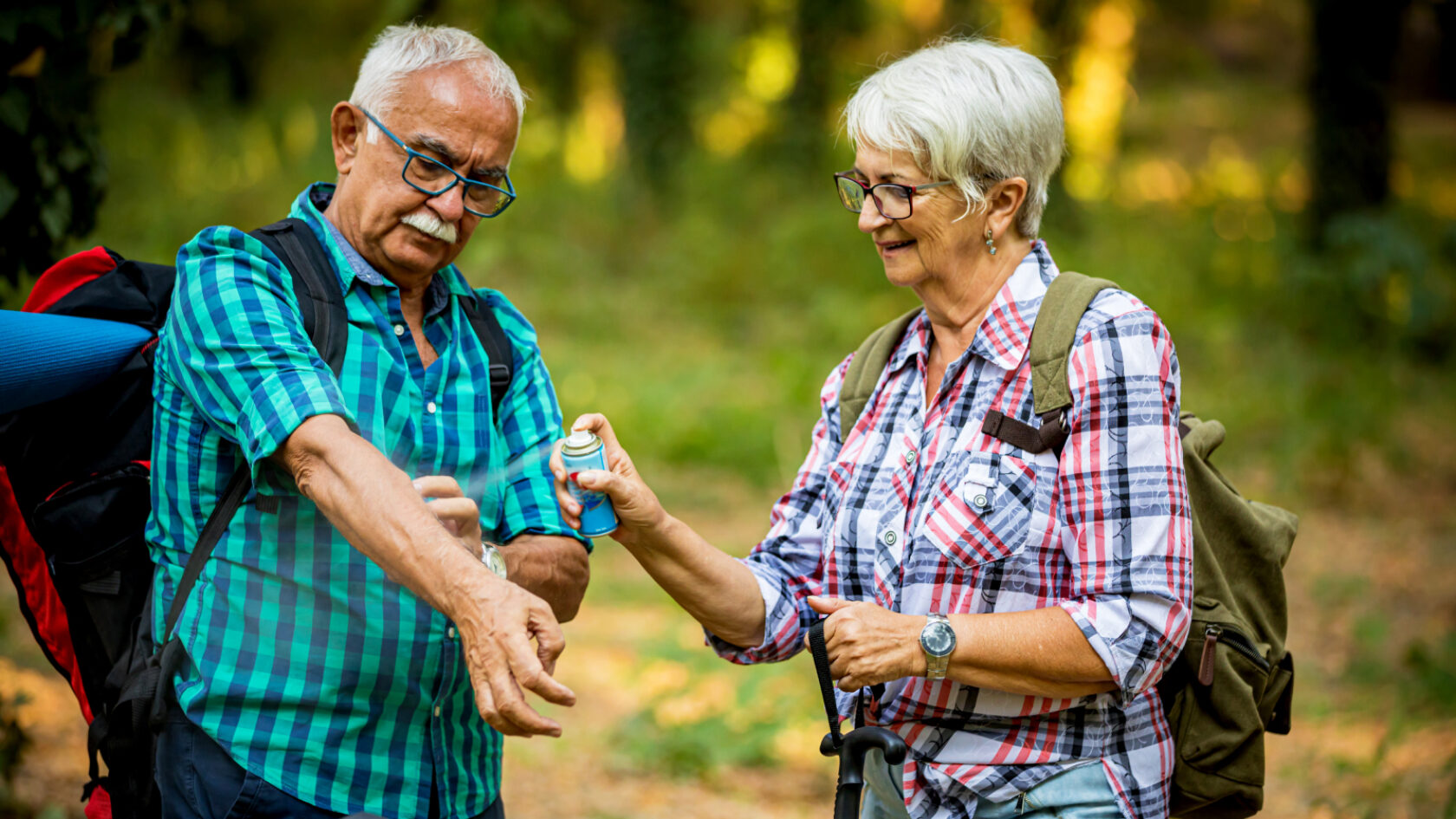 A woman helps a man apply bug spray while out hiking.