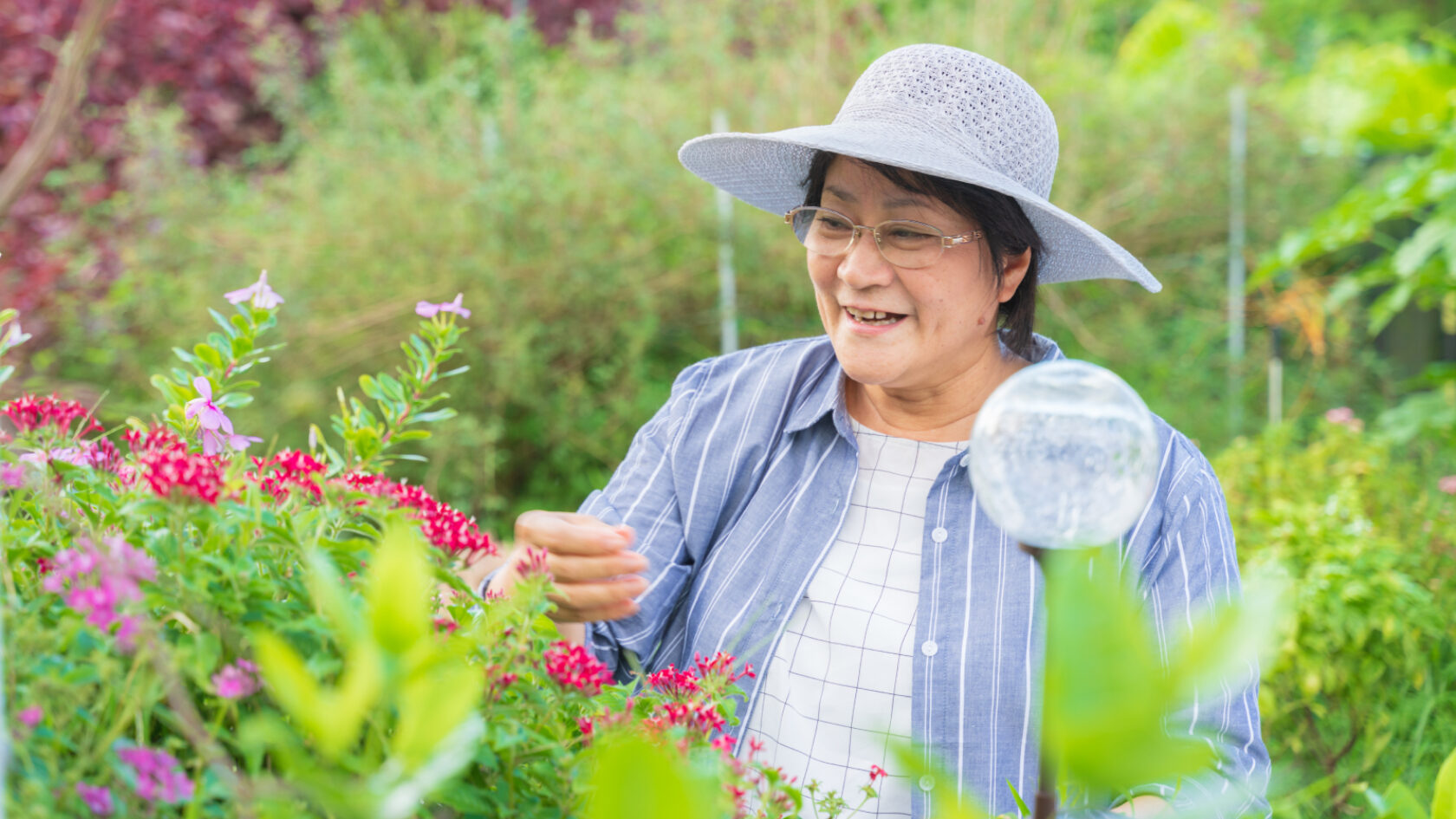 A woman tends her garden wearing a wide-brimmed hat.
