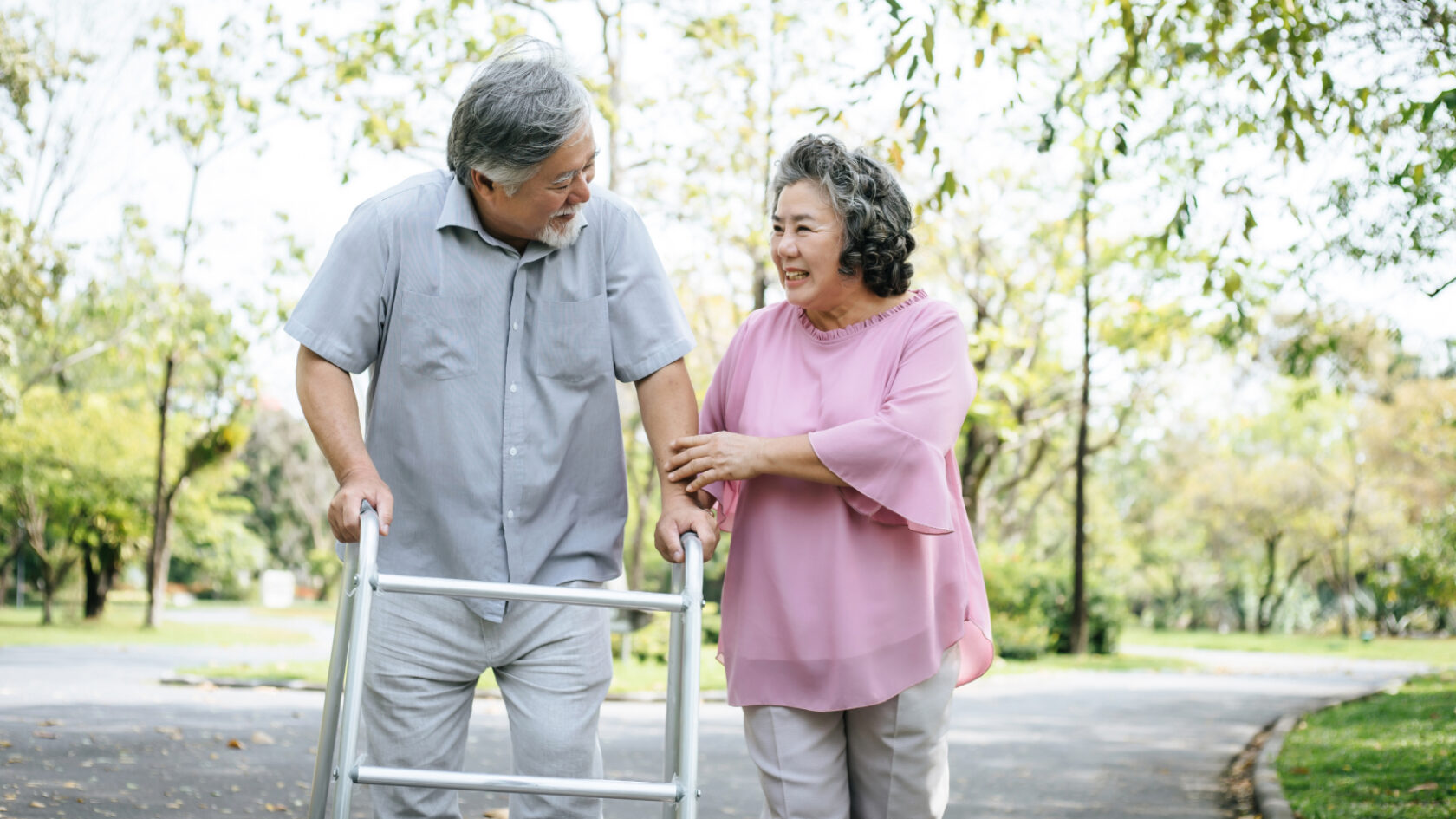 A woman supports a man using a walker during a walk outside.