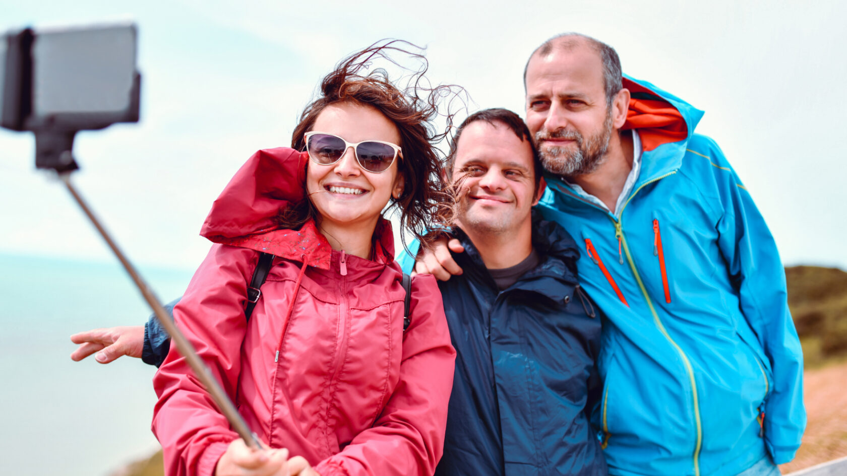 A family takes a selfie on a windy day by the water.