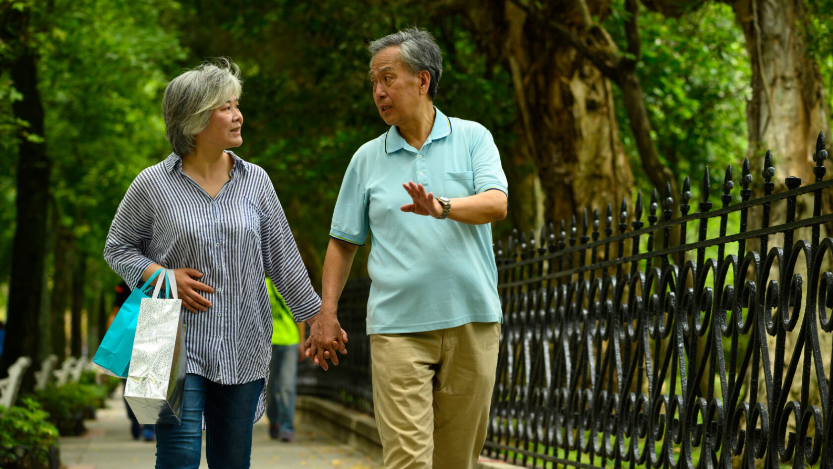 A couple walks in a park holding hands.